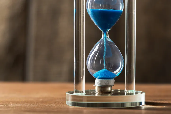 A blue hourglass mid-flow, close up on a wooden surface