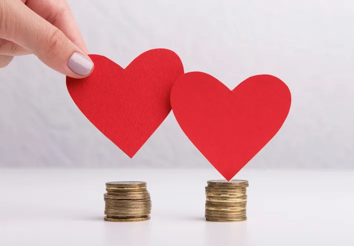 Two paper hearts balanced on two stacks of coins, symbolising weighing love and money